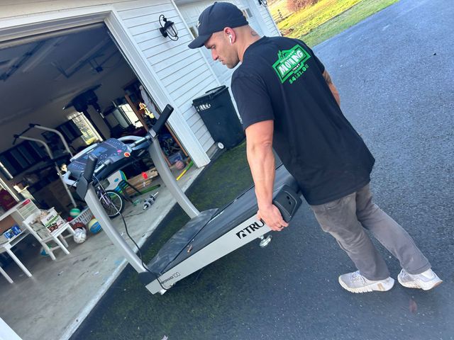 Mover wearing a Pacific Northwest Moving shirt handling an item near a garage
